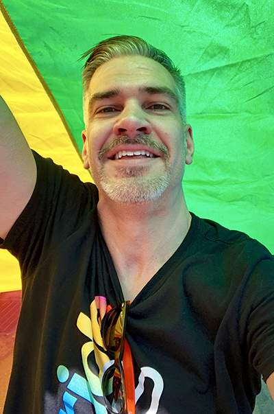 Close up of Keith Willard standing underneath a Pride flag