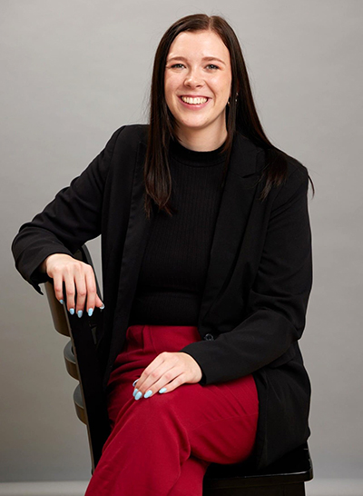 Hannah St. Clair seated wearing black blazer and red pants