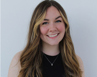 A woman with long hair and a delicate necklace smiles directly to the camera.