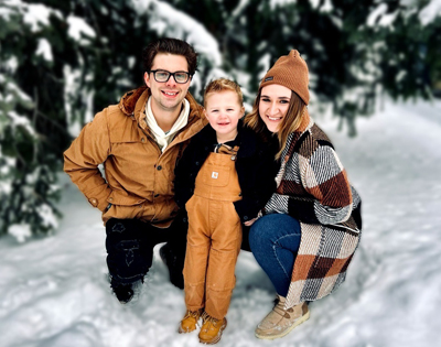 A family smiles together for a photo, surrounded by a snowy landscape.