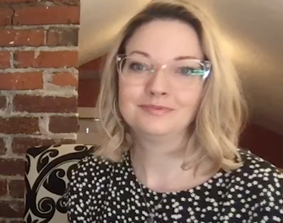  A woman wearing glasses is seated at a desk directly looking at camera.