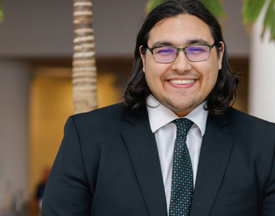 A man with glasses smiling and dressed in a suit jacket and tie.