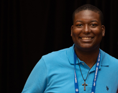 A man in a blue shirt smiling and looking directly at the camera.