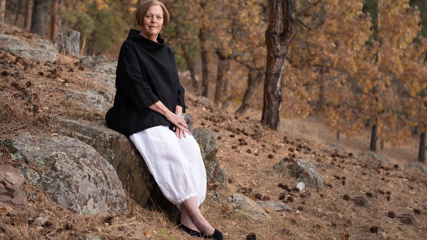 A woman seated on a rock surrounded by trees and natural greenery.