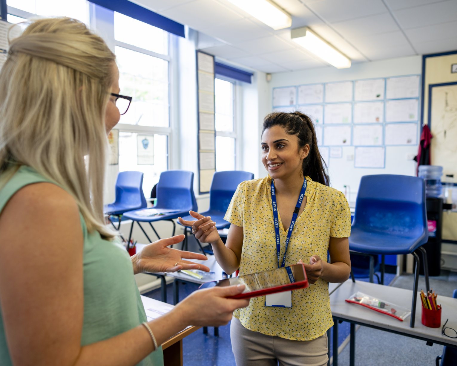 photo of blonde-haired educator speaking to a brown-haired educator in a classroom