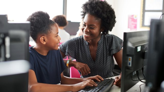 Black teacher and student work together in school computer lab