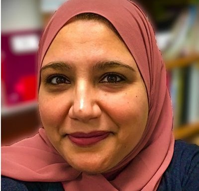 A female teacher wearing a hijab and smiling at the camera.