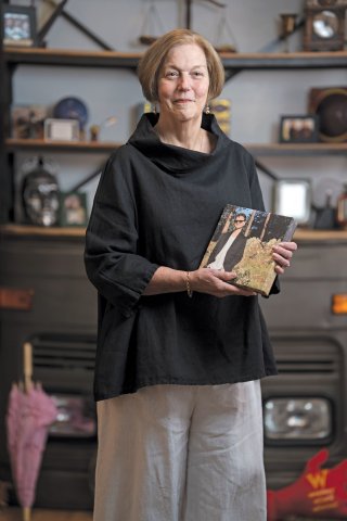 Mary Jane Chiles stands, holding a framed photograph of her grandson and looking directly into the camera