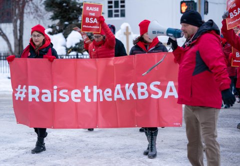 3 people marching in red jackets holding banner in the snow