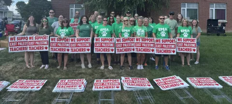 East Palestine Teachers standing in matching shirts and holding yard signs