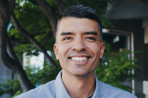 A man stands in front of a tree, smiling warmly.