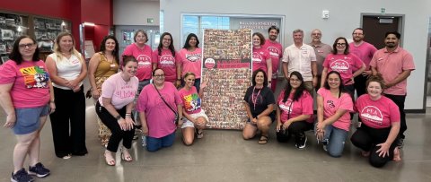 Several people dressed in pink shirts stand together, smiling for a group photo.